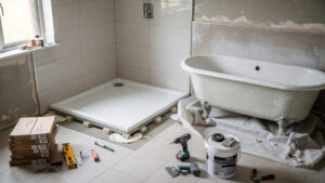 Salle de bains familiale en rénovation avec ancienne baignoire déposée, receveur de douche extra-plat et outils d’artisans éclairés par la lumière naturelle.
